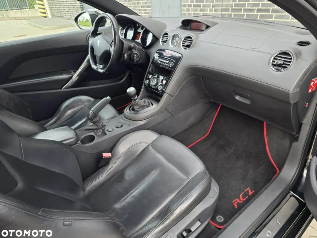 Wnętrze Peugot RCZ z czarną skórzaną tapicerką i czerwonymi akcentami na dywanikach.