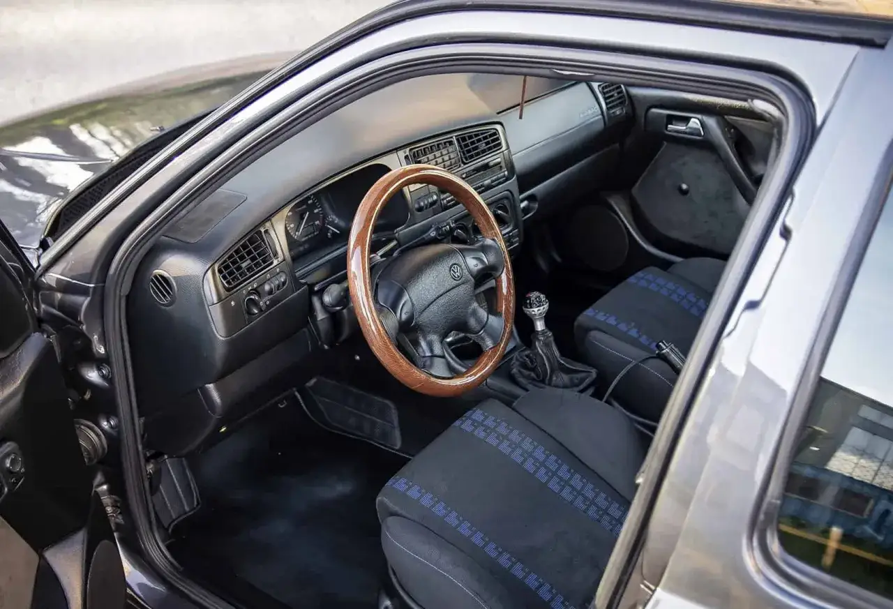 Wnętrze klasycznego VW Vento z drewnianą kierownicą i sportowymi siedzeniami w niebieskie paski.