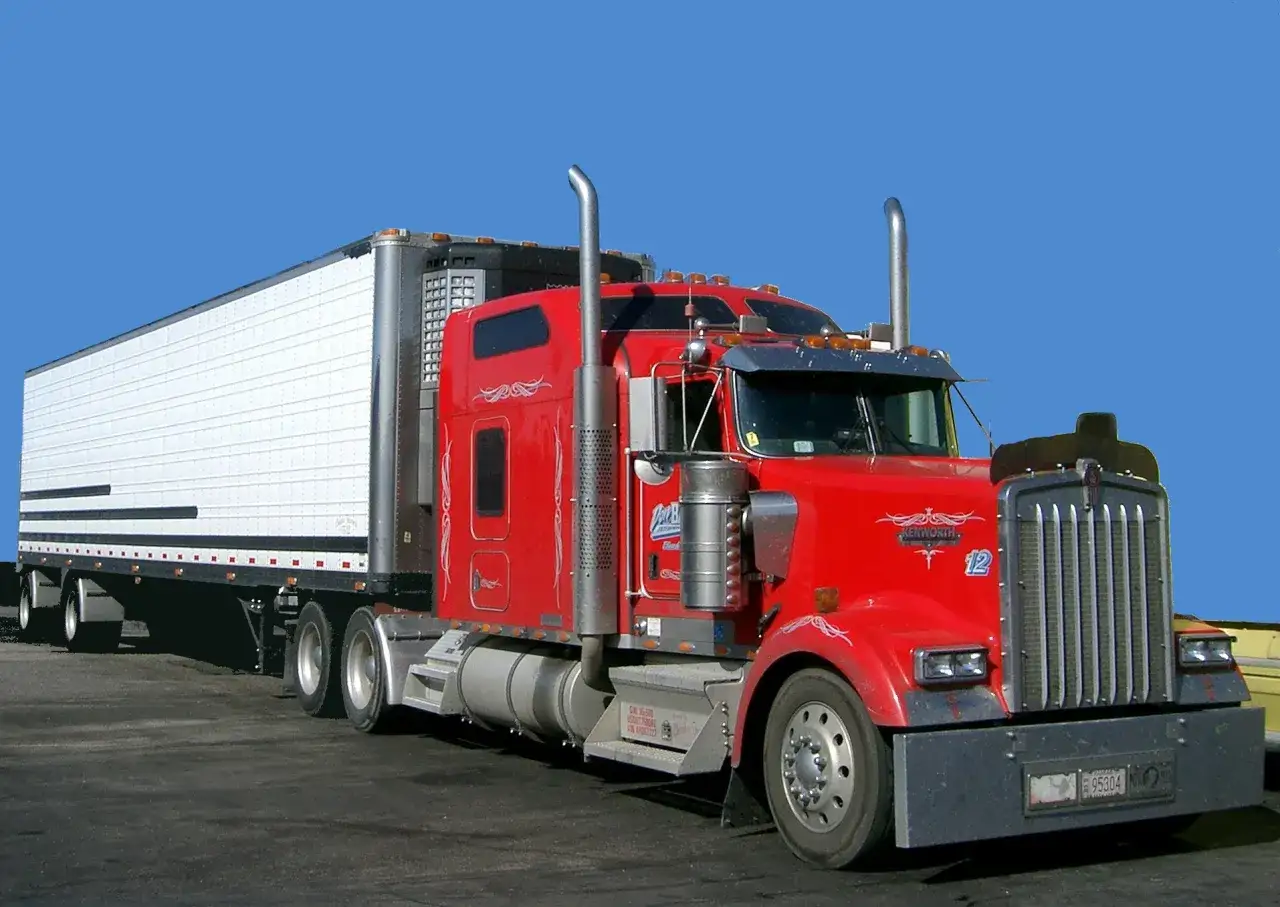 Czerwony Kenworth W900 z naczepą chłodniczą, gotowy do długiej trasy.