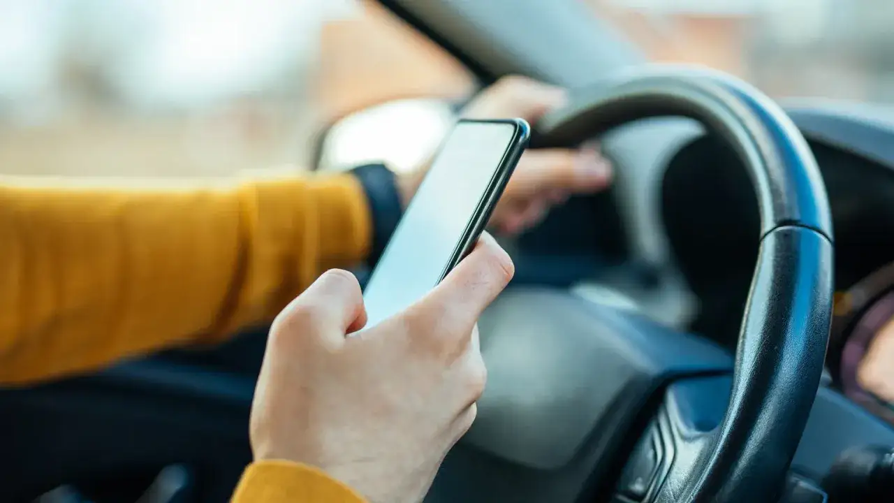 Ręka trzymająca telefon za kierownicą. Uważaj, bo to grozi mandatem za telefon.