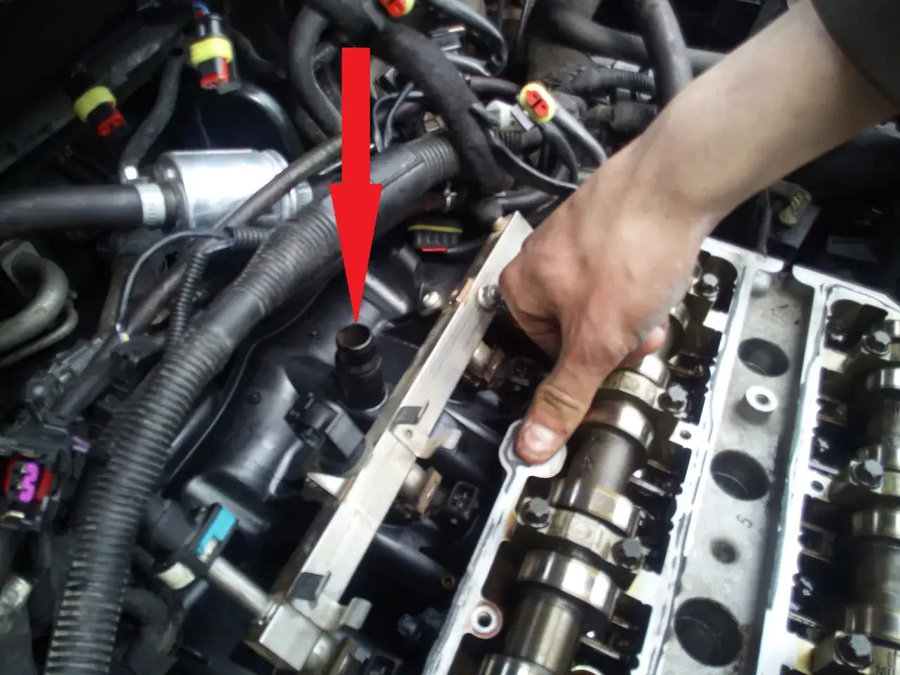 Ręka mechanika wskazuje na miejsce awarii, być może związanej z błędem dtc p1113 opel. Widoczny jest fragment silnika z wałkami rozrządu.