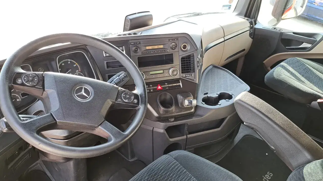 Wnętrze kabiny ciężarówki Mercedes Actros MP4. Widoczna kierownica, deska rozdzielcza z radiem i przyciskami, fotel pasażera.
