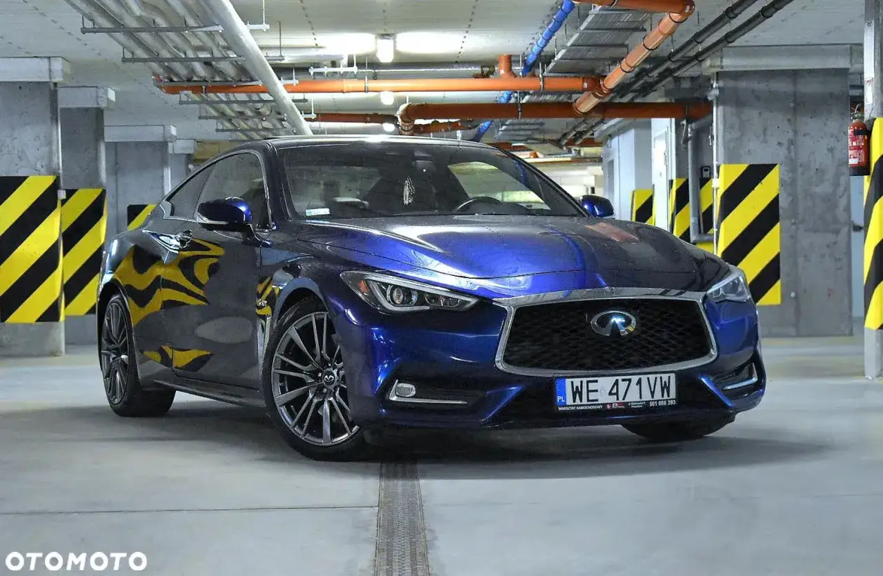 Błękitne infiniti auto coupe z przyciemnianymi felgami stoi na parkingu podziemnym, odbijając żółto-czarne słupki.
