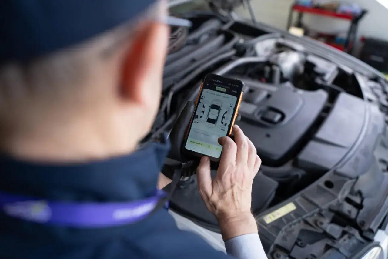 Mechanik sprawdza na telefonie kody błędów samochodu, analizując schemat uszkodzeń.