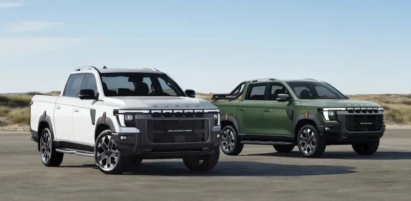 Dwa SsangYong pickup: biały i zielony, stojące na tle plaży i wydm.
